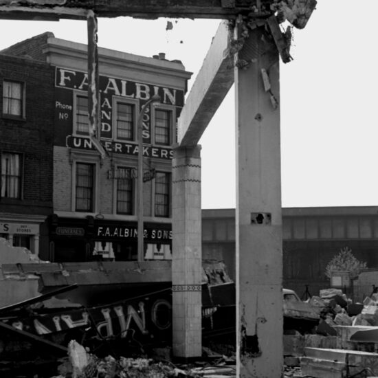 The premises of F. A. Albin and Sons, Undertakers, can be seen behind a destroyed building in Bermondsey, south London, 10 April 1961