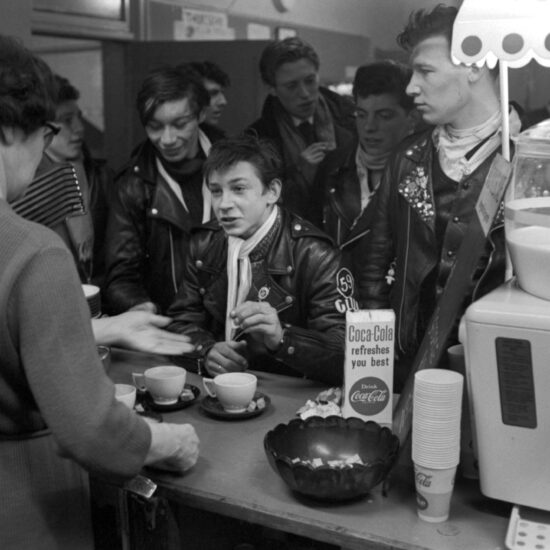 Members of the 59 Club bikers club queue at the counter and chat with the woman serving cups of tea at a cafe in Paddington, west  London, circa 1964