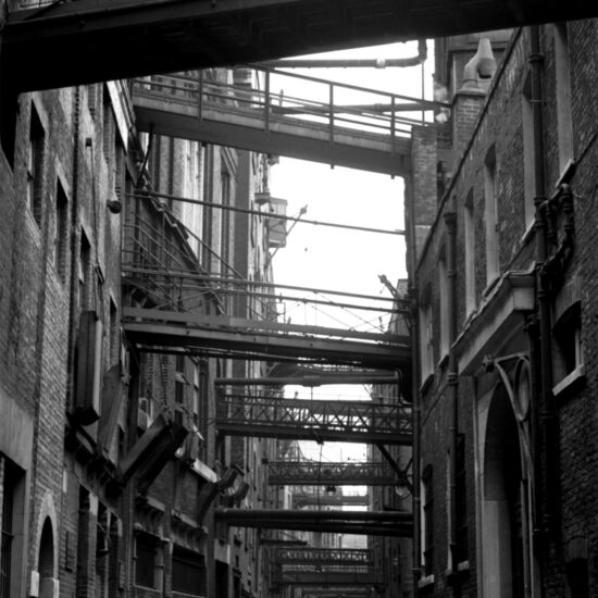 A deserted street in London’s Docklands area: metal walkways above ground link industrial warehouse buildings along the river Thames, London circa 1961