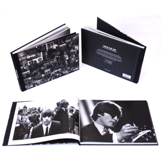 Three copies of the book FROM THE HIP - Photographs by JOHN 'HOPPY' HOPKINS 1960-66 on a white background. The front and back covers are visible on two of the books standing upright, and an open copy of the book in the foreground features images of three of the Beatles on one page and John Lennon on the other.