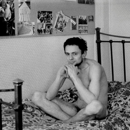 John Hoppy Hopkins at Westbourne Terrace, sits naked on a bed in front of an ideas board, circa 1962, West London