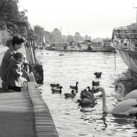 A woman and her young daughter feed the ducks and swans on the river Thames in Kingston, west London, circa 1961
