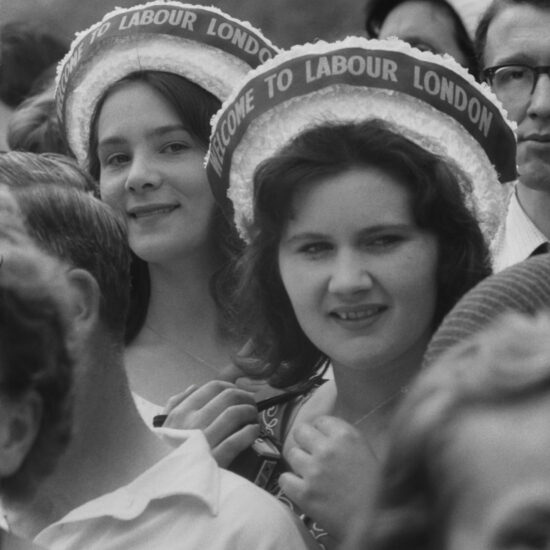 During the 1962 Festival of Labour in Battersea Park, two women wearing Welcome to Labour London hats stand in the crowd