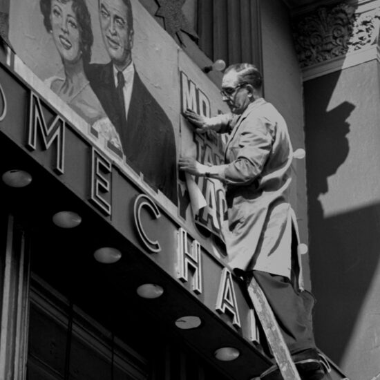 A man up a ladder pastes an advert for the film ‘Mr Hobbs Takes a Vacation’ ft. Jimmy Stewart and Maureen O’Hara, above the main entrance at The Mechanics Cinema in Nottingham, England 1962