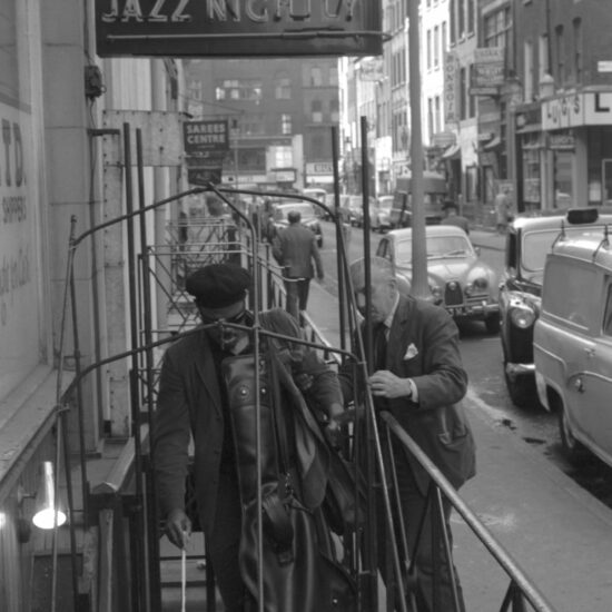 Followed by Ronnie Scott, American jazz multi-instrumentalist Rahsaan Roland Kirk carries his saxophone over his shoulder as he descends the exterior stairs of Ronnie Scott’s Jazz Club at 39 Gerrard Street, London, circa 1963