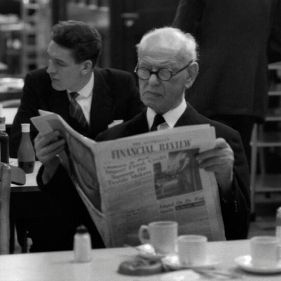 In the Stock Exchange canteen an elderly white male stockbroker reads a financial newspaper (Financial Review) with other colleagues in the background, on May 24 1961