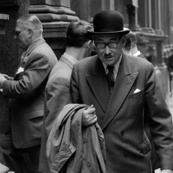 A middle-aged man wearing a moustache and bowler hat walks past the Stock Exchange Visitor's Gallery entrance on May 24 1961